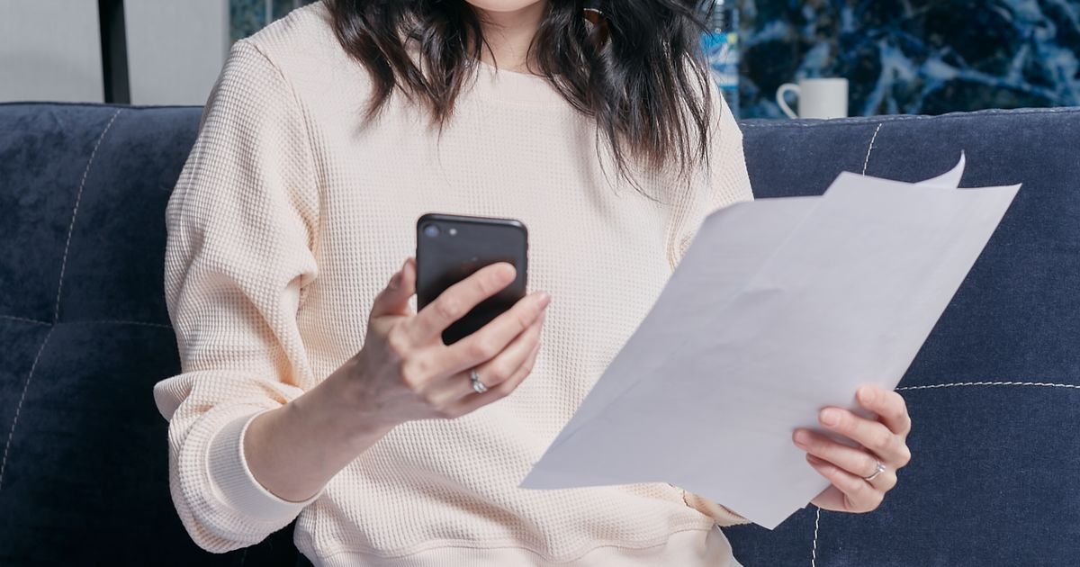 소파에 앉아 스마트폰과 서류를 함께 확인하는 모습